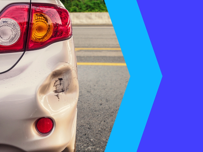 Rear bumper of dented cars with visible damage from collision on a road, awaiting repair.