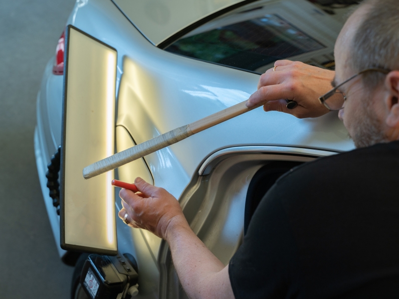 A technician repairing a dent in car using a specialised tool in a paintless dent removal process.