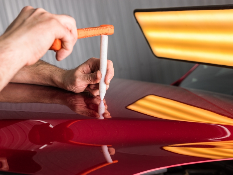 Performing paintless dent repair at home on a red car bonnet using a tapping tool.